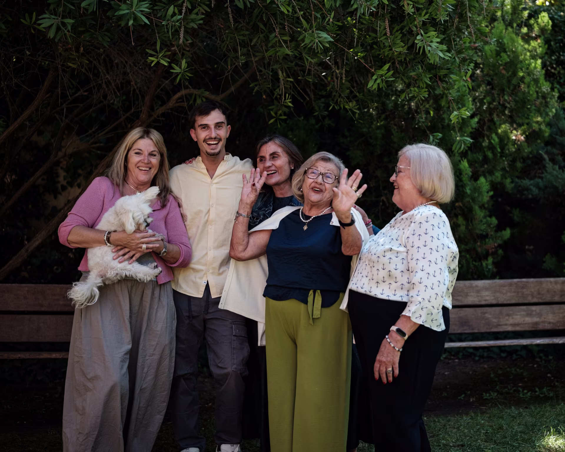 Una familia y un perro sonríen y saludan en un parque.