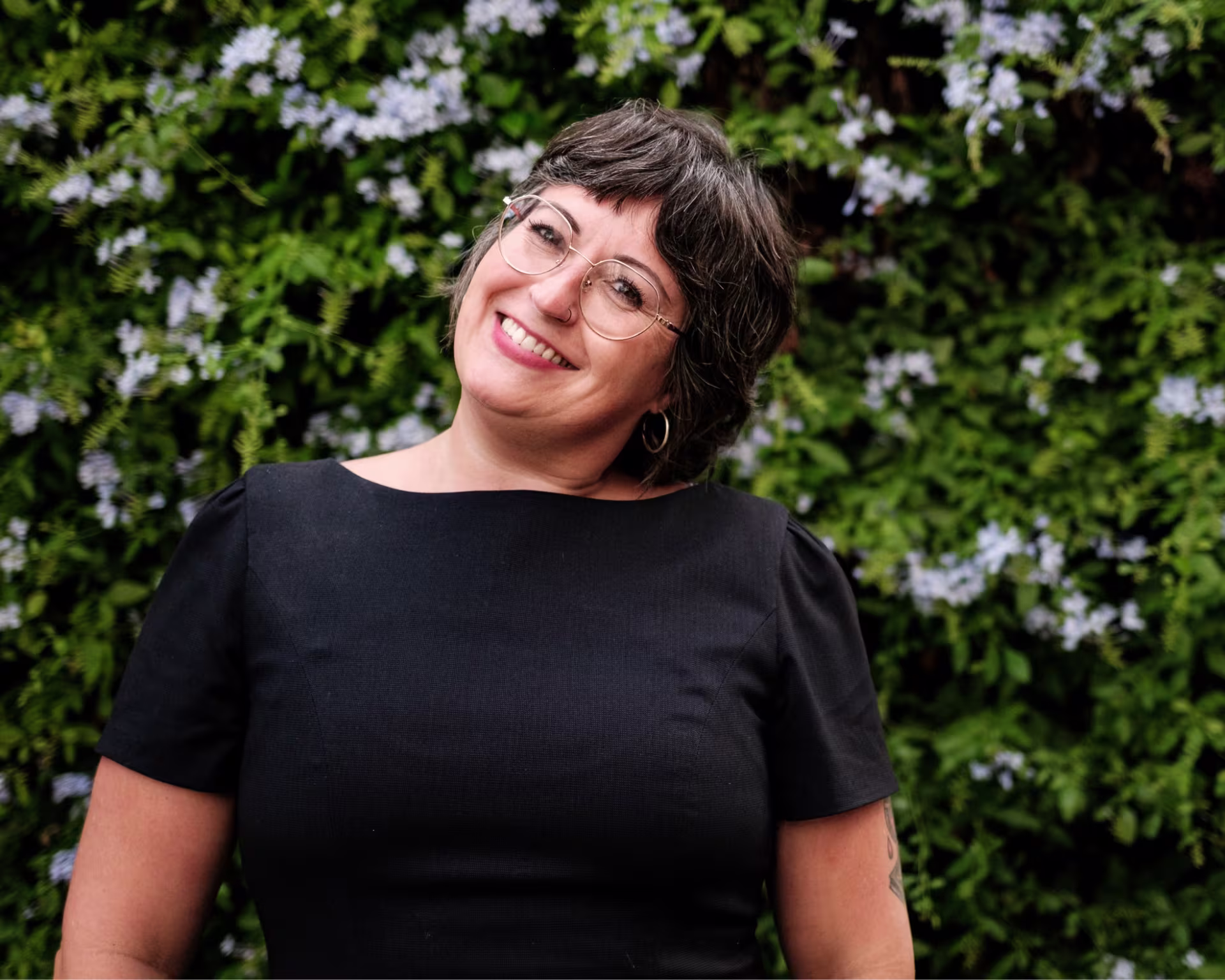 Mujer sonriendo con gafas y piercing, fondo de flores.