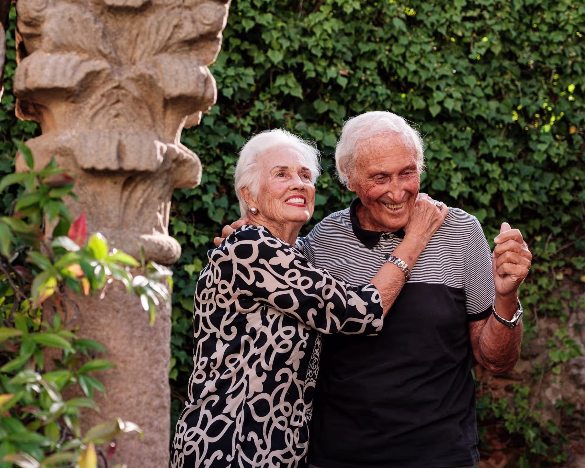 Dos personas mayores sonrientes en un jardín.