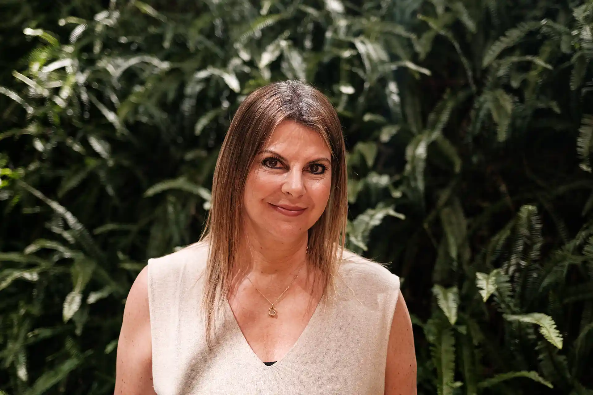 Mujer sonriendo con fondo de plantas verdes.