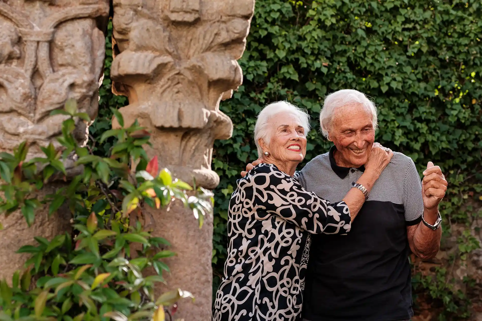 Una pareja senior sonríe y abraza en un entorno verde.