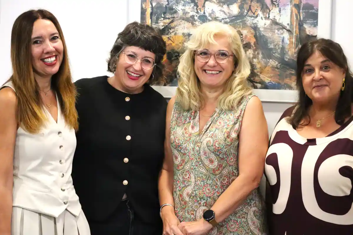 Cuatro mujeres sonríen frente a una pintura abstracta.